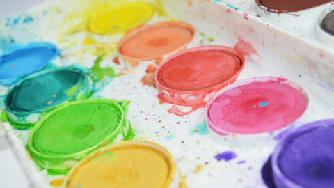 Brightly colored paints in a white paint pan, with lots of paint splatters.