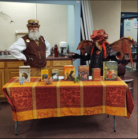 Man standing behind a table with books that have photos of dragons on them.