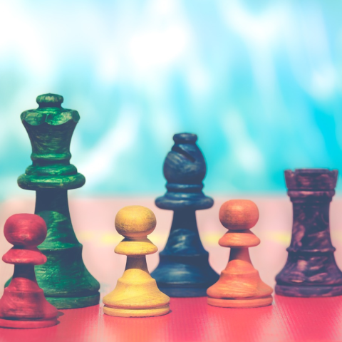 Brightly colored chess pieces on a red board.