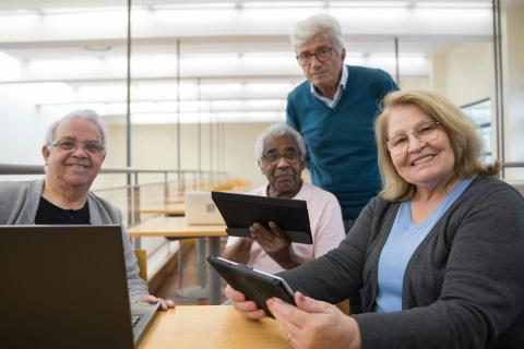 4 older adults in a computer classroom, smiling for the camera