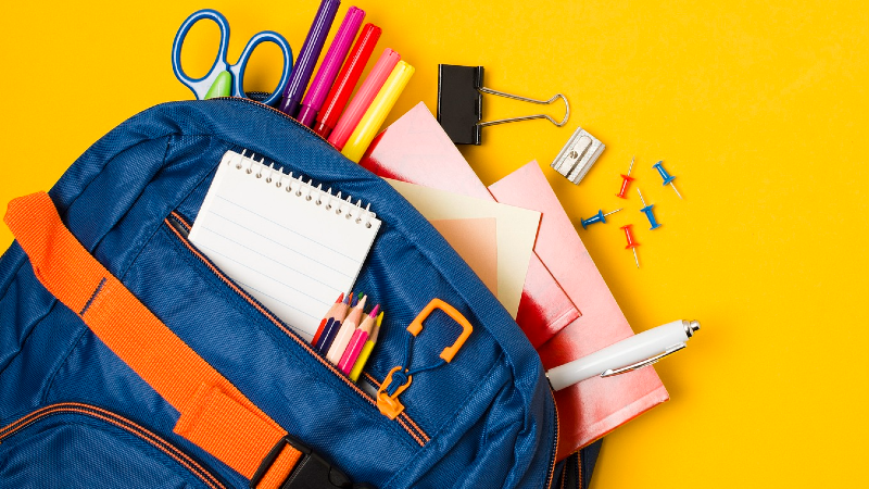 A blue backpack stuffed with school supplies, including scissors and markers.